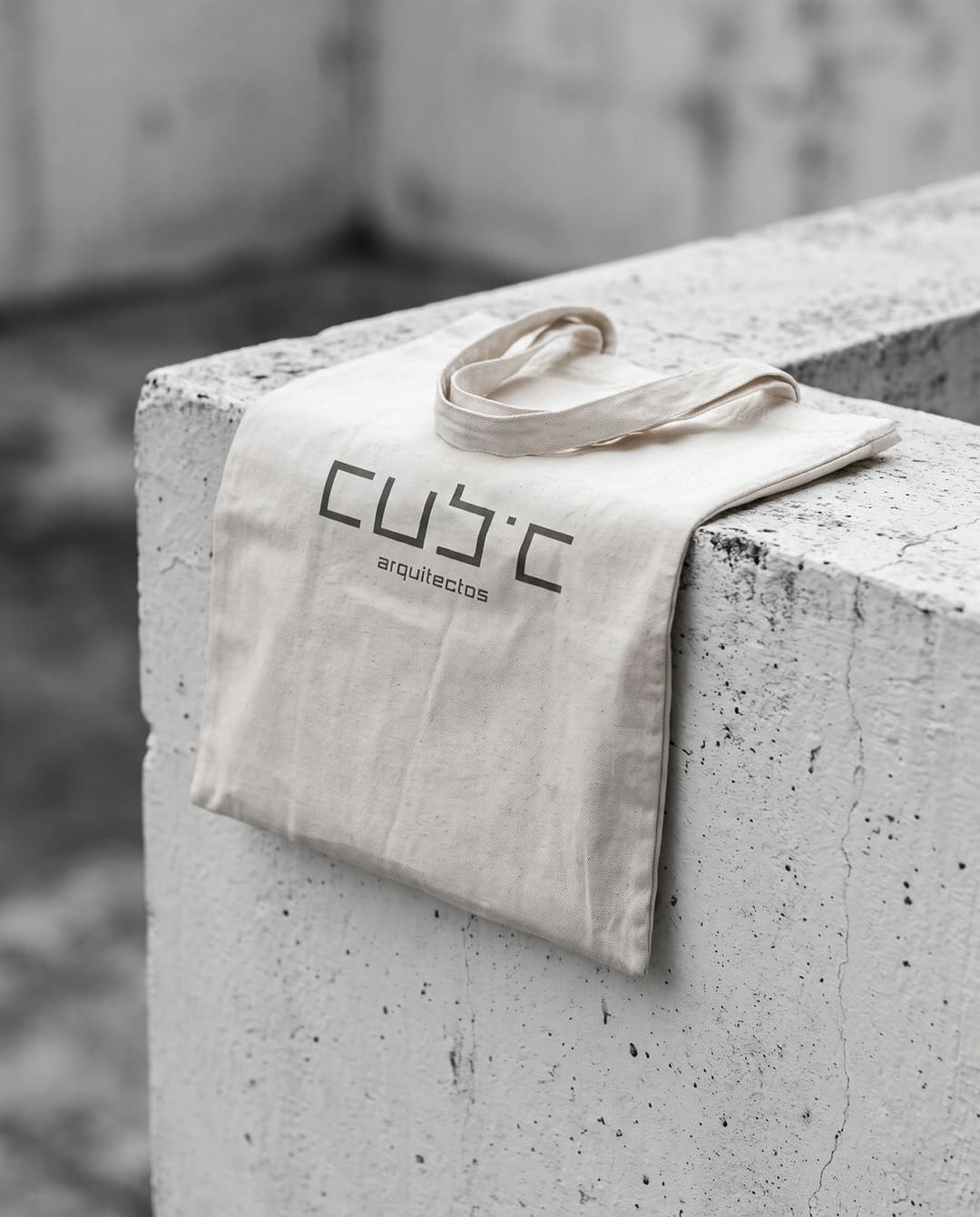 Uma tote bag crua dobrada sobre um muro de betão, com o logótipo da Cubic a cinzento-escuro.