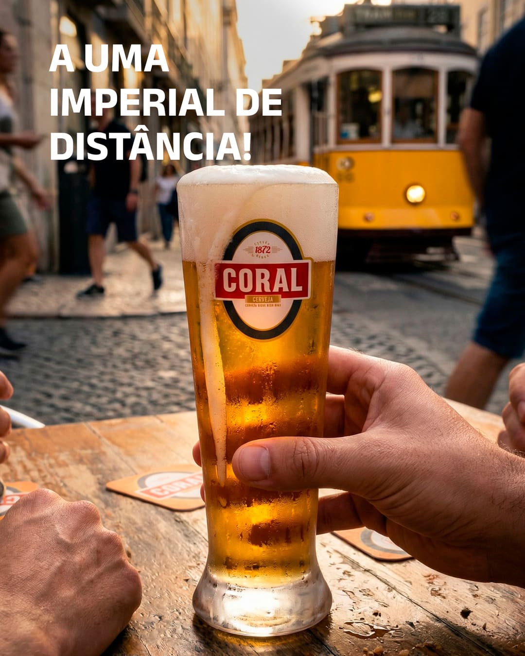 Uma imperial Coral numa mesa de esplanada numa rua de calçada de Lisboa, com o eléctrico amarelo ao fundo. Em cima, «A uma imperial de distância!».