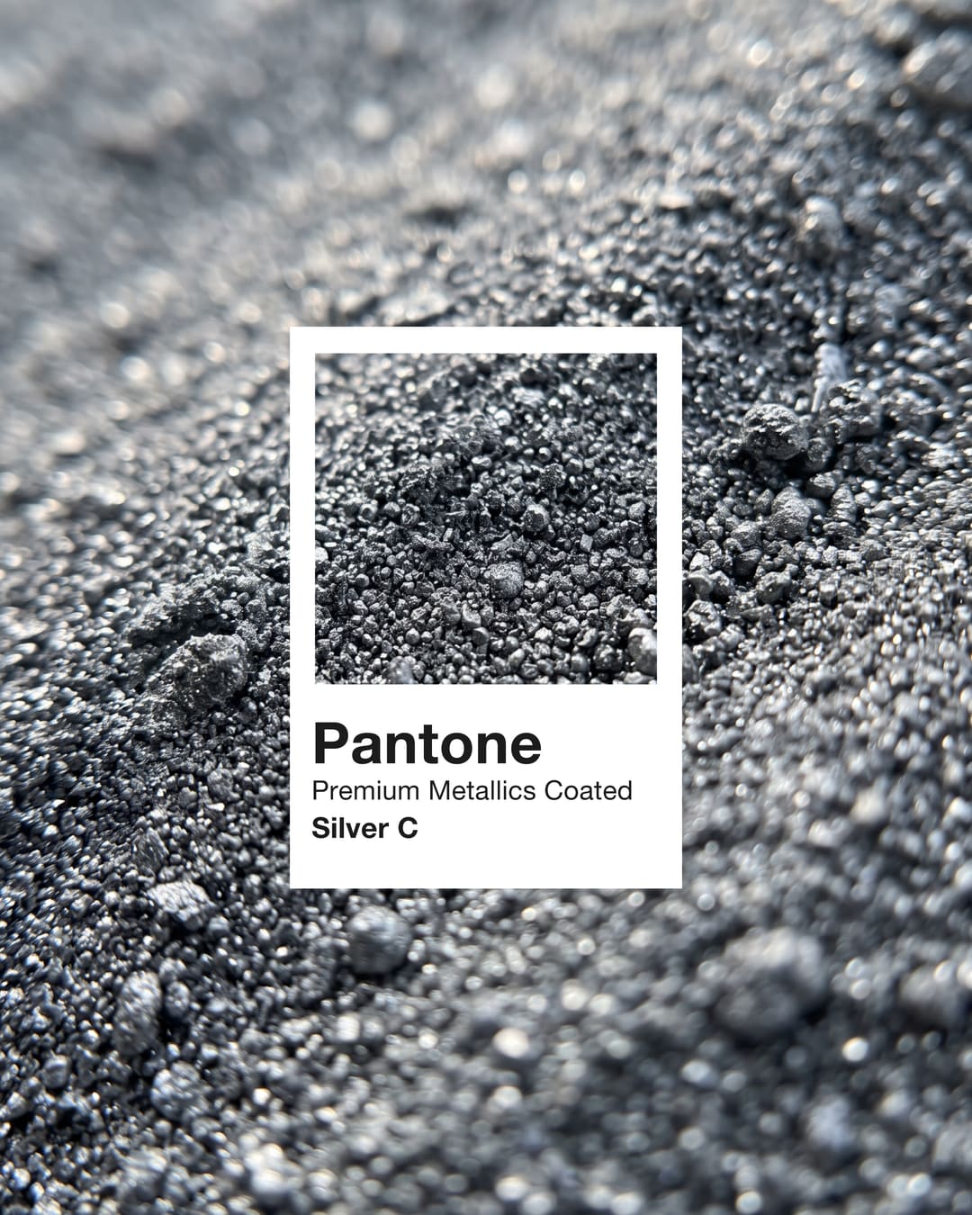 Uma amostra Pantone Premium Metallics Coated Silver C sobre grânulos prateados.