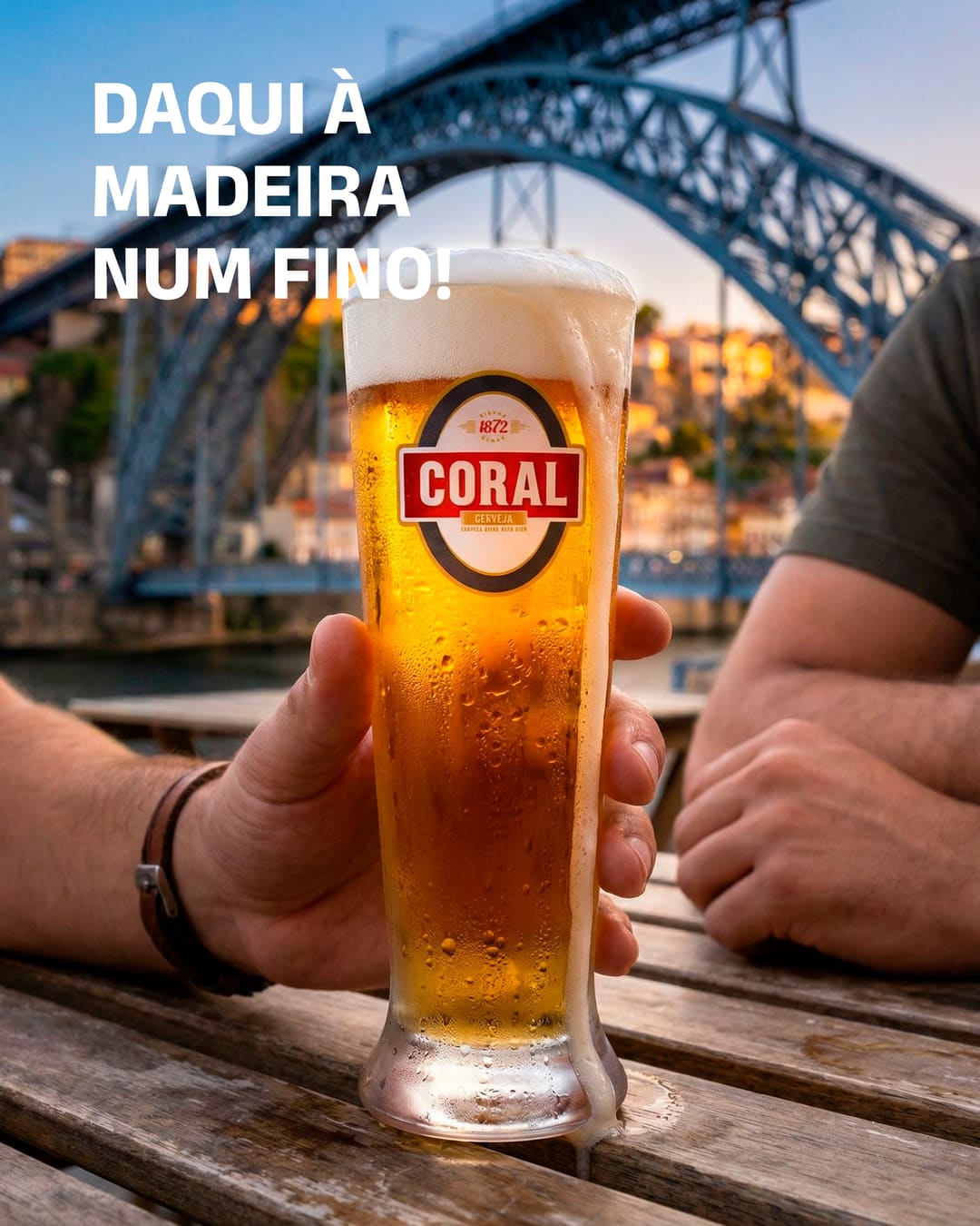 Um fino Coral numa mesa de madeira junto ao Douro, com a ponte D. Luís ao fundo, ao fim da tarde. Em cima, «Daqui à Madeira num fino!».