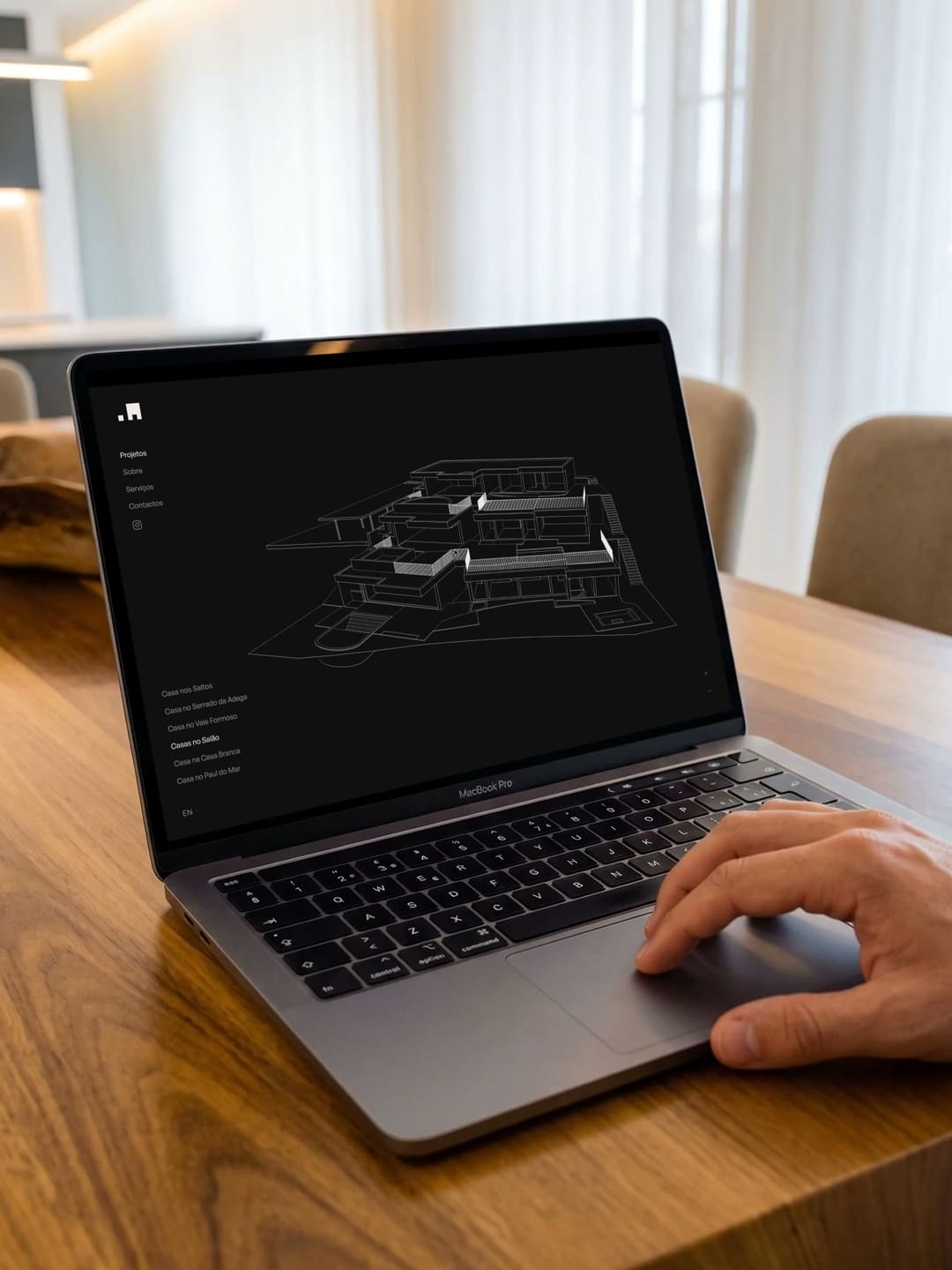 Um portátil sobre uma mesa de madeira com o website dos AA: o desenho de linhas de uma casa roda no ecrã escuro.