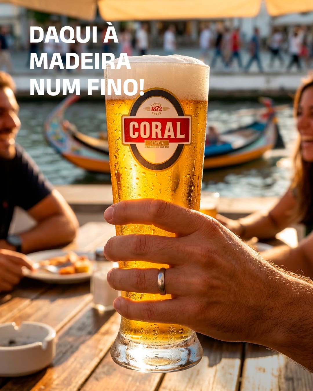 Uma mão levanta um fino Coral numa esplanada junto à ria de Aveiro, com moliceiros ao fundo e amigos a sorrir à mesa. Em cima, «Daqui à Madeira num fino!».