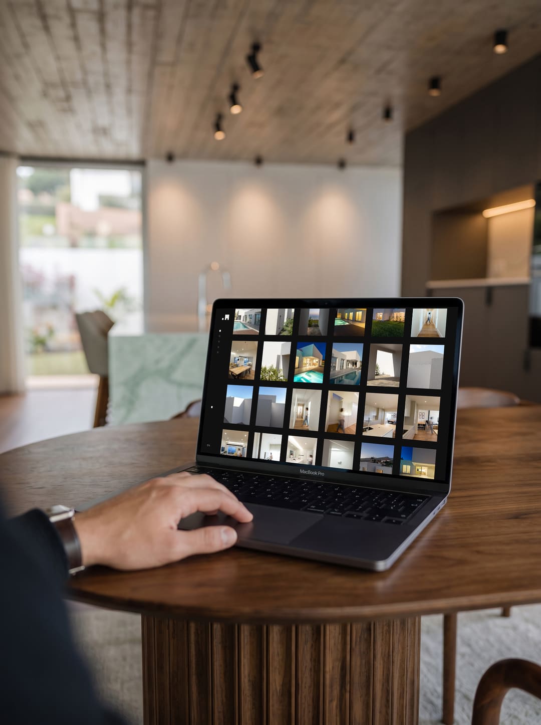 Um portátil numa mesa redonda com o website dos AA: uma grelha de fotografias de casas brancas, piscinas e interiores.